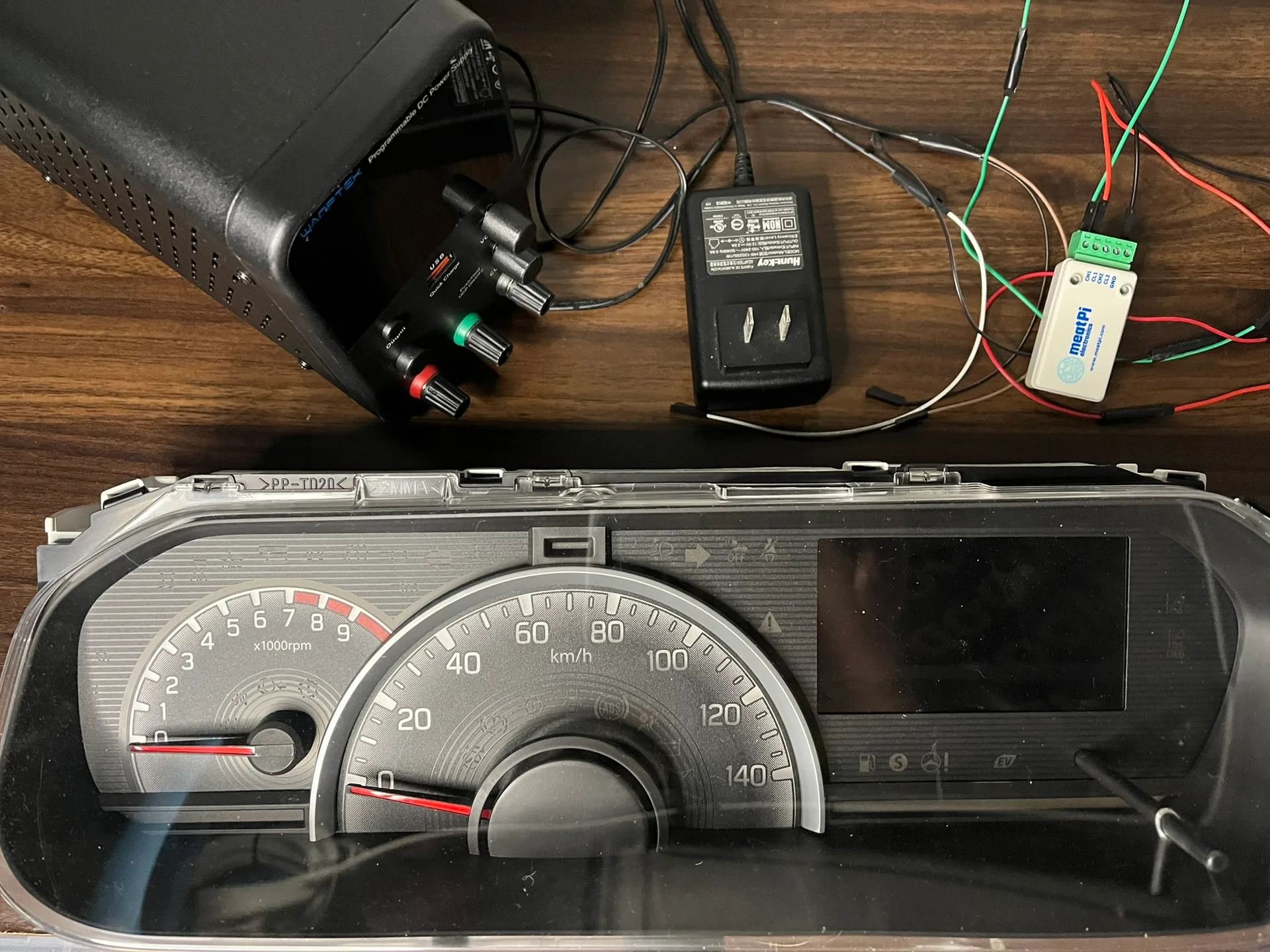 図1：検証に使用したツールとインストルメントクラスター（左からWanptek製可変電源、12V電源アダプター、meatPi製USB Dual-CANアダプター、スズキ・ワゴンR MH55S）